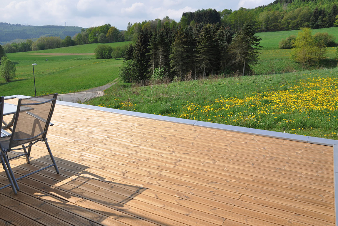 Eine Terrasse aus Thermokiefer bildet eine perfekte Einheit mit der Natur, dem Ausblick auf den Wald und blühende Wiesen.